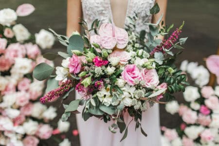 Woman holding in hands big wedding bouquet in rustic style. Greens, pink and white roses, coral anthurium. Pastel colored.